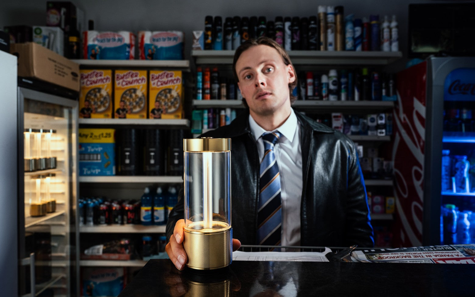 Man holding a Buster & Punch Takeout lamp in Brass in a store setting with shelves stocked with products.