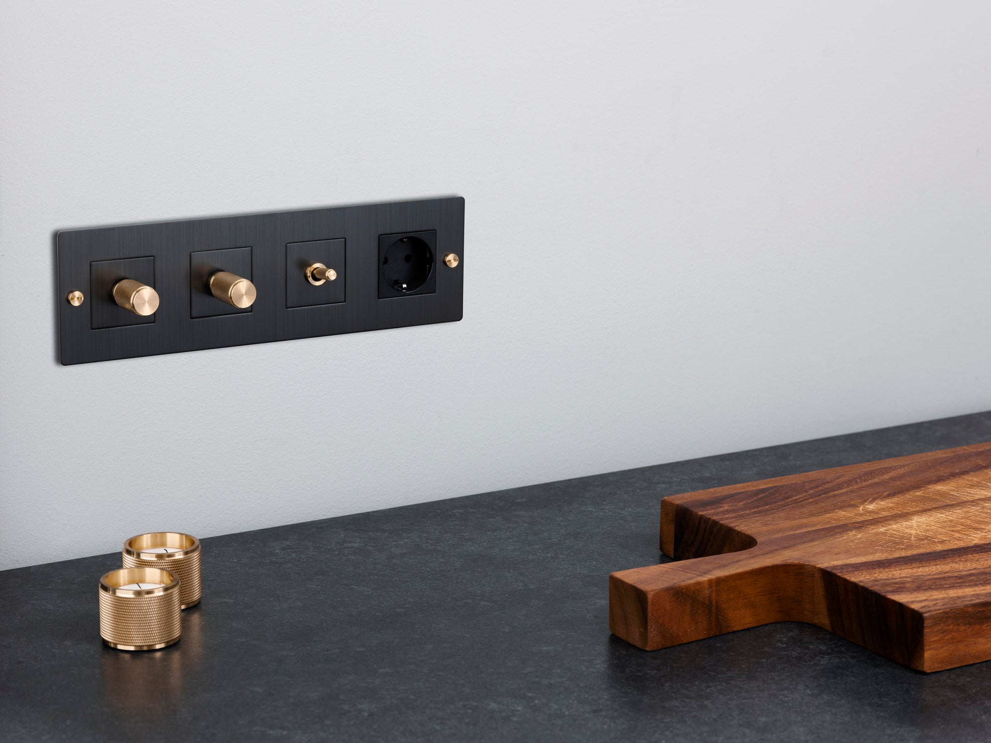 A Buster + Punch 4G module with dimmers, toggle and socket with brass details on a grey wall