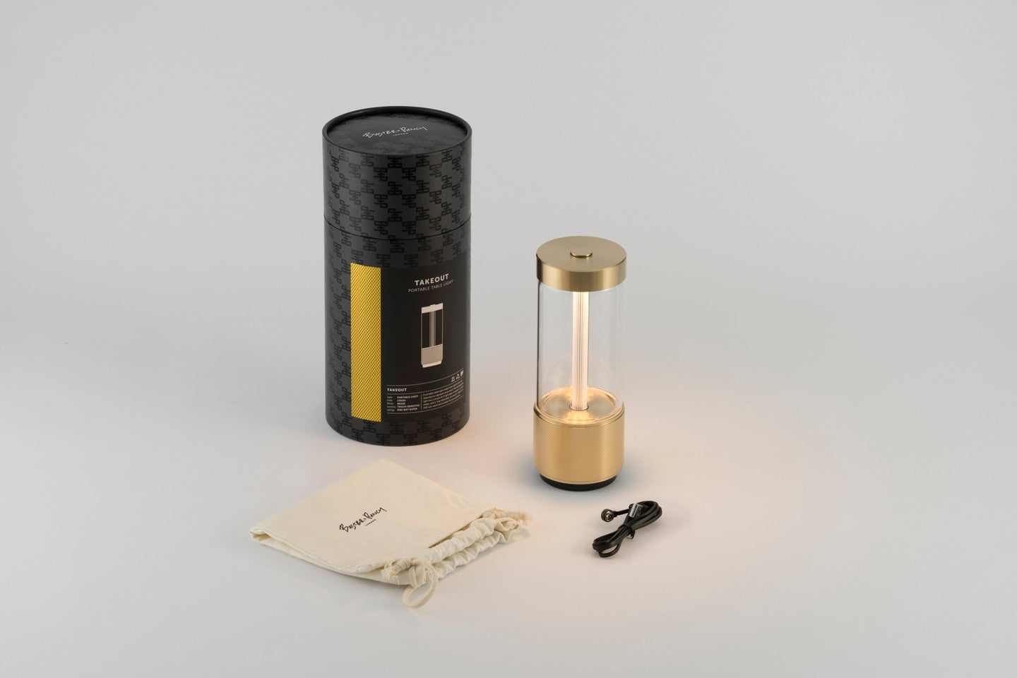 Buster &amp; Punch Takeout lamp in Brass with packaging, drawstring bag, and USB cable on a light gray background